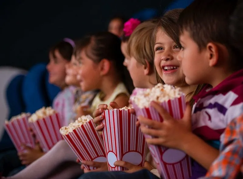 Young kids sat in a cinema eating popcorn.