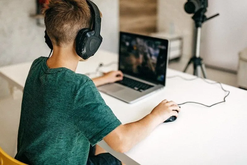 Young boy recording a vlog of him playing on his laptop with headphones on.