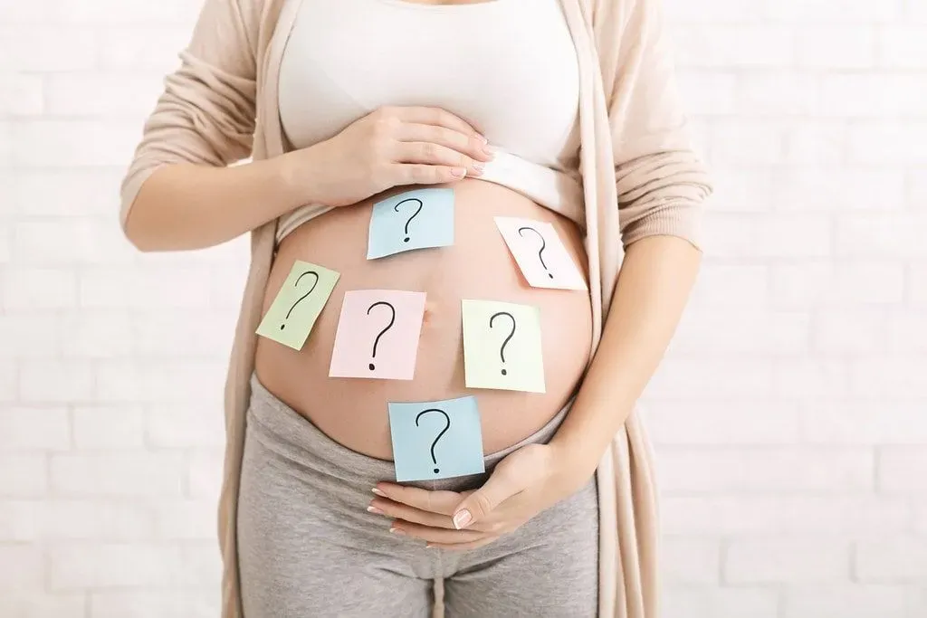 Expectant mother with sticky notes with question marks written on them stuck on her baby bump.