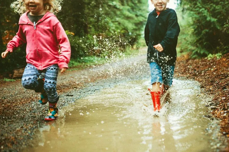 kids wearing rain boots splash and play in a big mud puddle