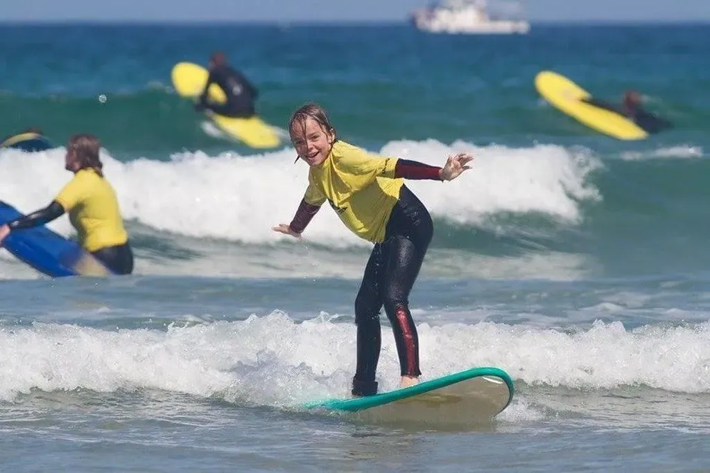 Kid standing on a surfboard in the sea riding the waves.