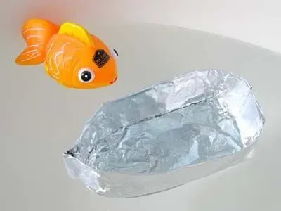 An aluminium boat and orange toy fish floating in water.
