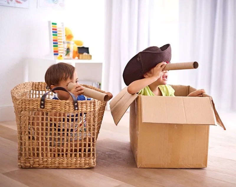 Two boys playing at home pretending to be pirates, sat in makeshift pirate ships made of a box and a basket.