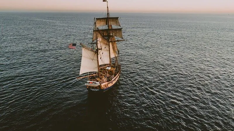 American pirate ship at sea sailing towards the horizon at sunset.