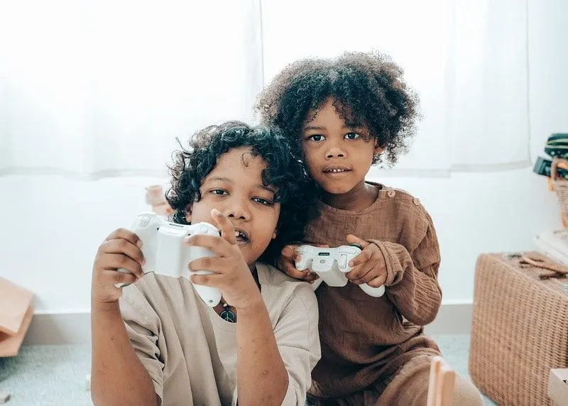 Two kids holding white games console controllers playing video games.