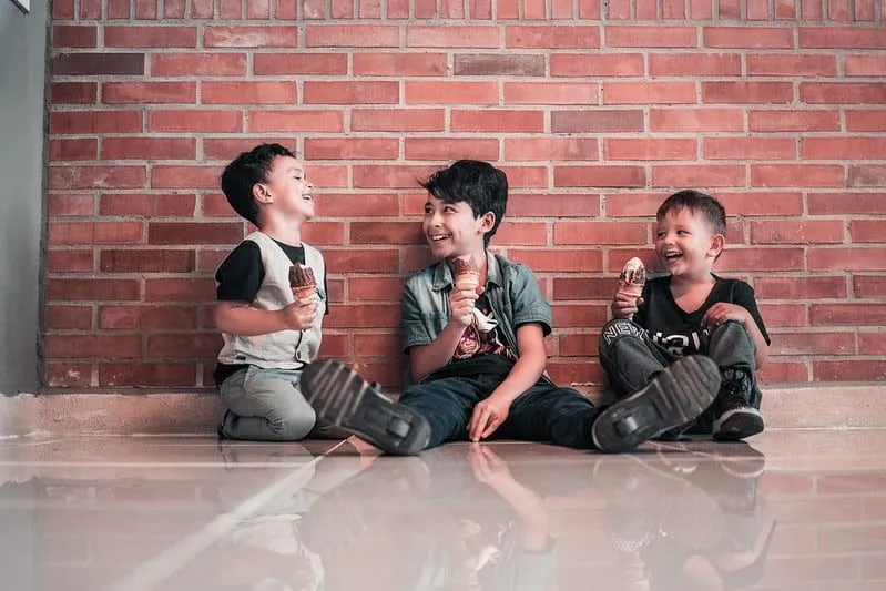 Three boys sat on the floor next to a wall eating ice cream and laughing at Shrek jokes.