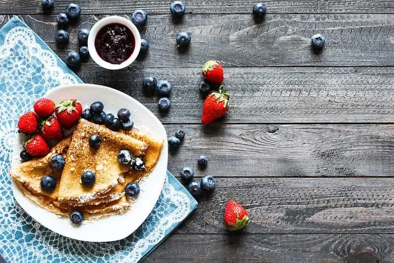 Plate of yummy folded crepes served with strawberries, blueberries and fruit compote.