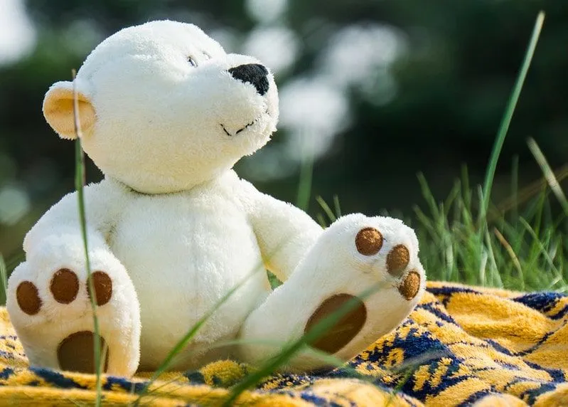 White teddy bear sat outside on a yellow picnic blanket.