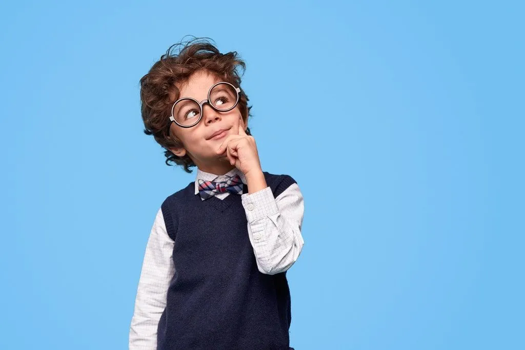 Smart-looking boy dressed in a shirt, sweater vest and bow tie and wearing glasses, thinks of corny riddles.