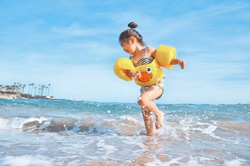 Girl splashing around in the sea at the beach wearing armbands and a floaty with a duck on it.