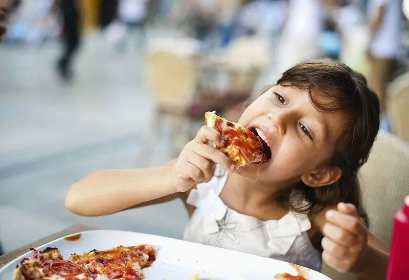 Young girl sat at the table in a restaurant eating a slice of pizza.