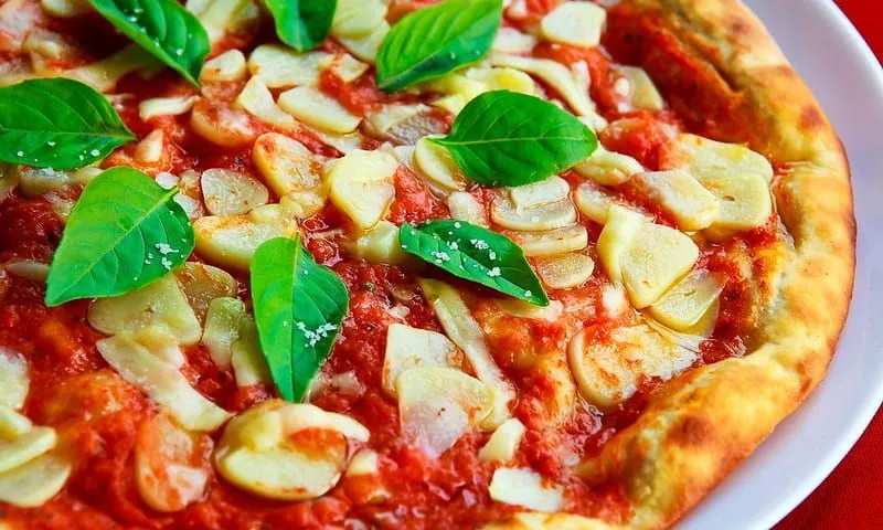 Vibrant looking pizza with garlic on top and basil leaves.