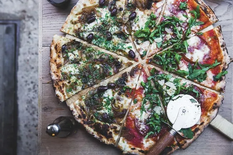 Half and half pizza cut into slices with a pizza cutter resting on the side of it.