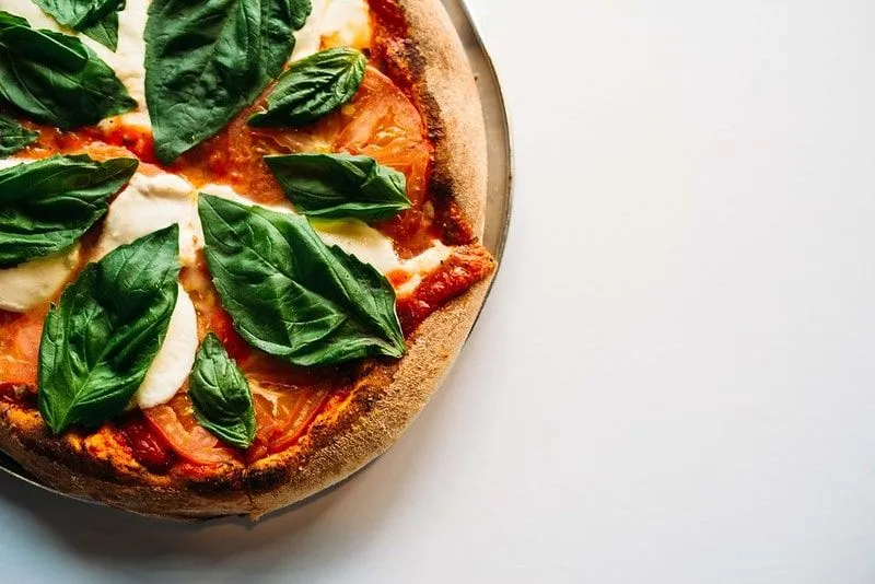 Homemade margarita pizza with big basil leaves on top.