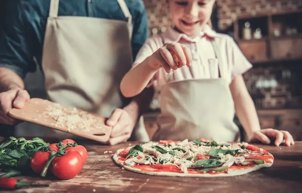 Dad and daughter in the kitchen making homemade pizza together.