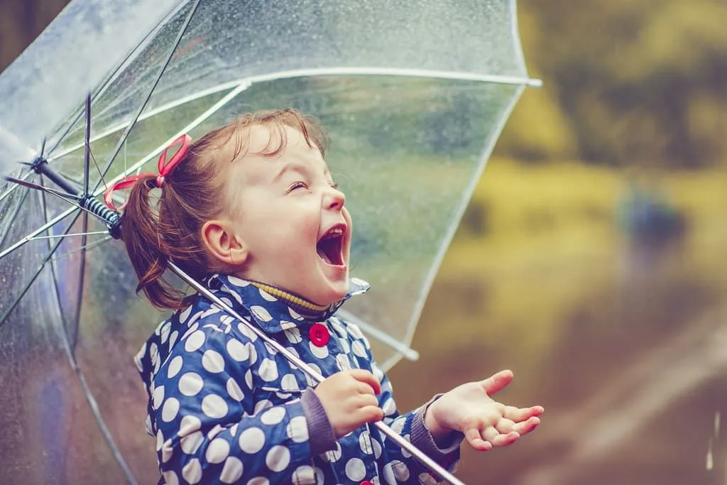 Little girl holding an umbrella laughing in the rain.