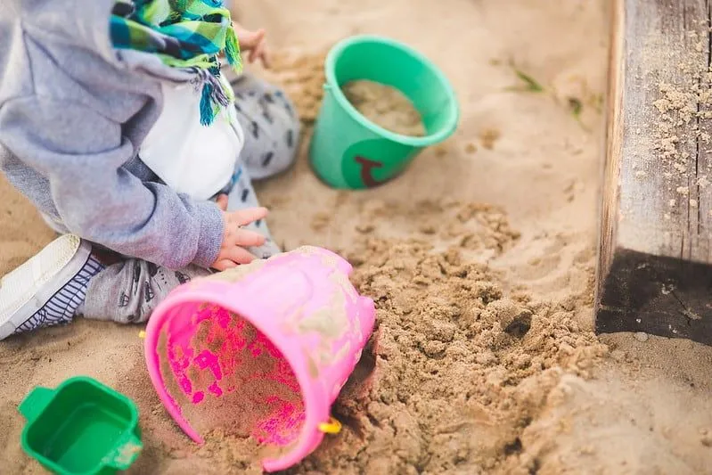 Toddler in the sand at the beach filling up buckets to make a sandcastle.