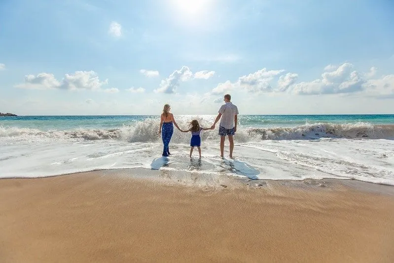 Family standing at the edge of the sea waves holding hands.