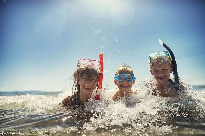 Kids sitting in the sea smiling and wearing snorkels.