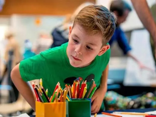 Young boy wearing a green t shirt choosing from two pots of coloured pencils.