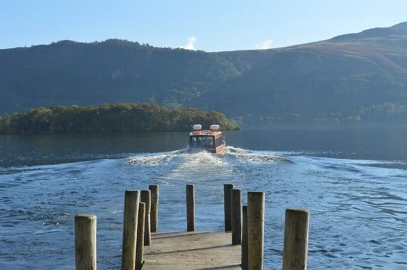 A boat moving away from the jetty on Windermere Lake overlooking the hills.