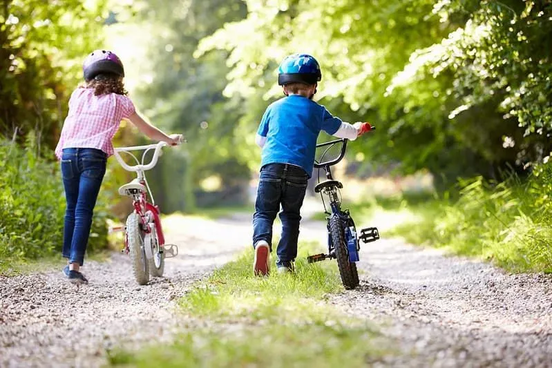 Little girl and boy pushing their bikes along the path on a nature trail.