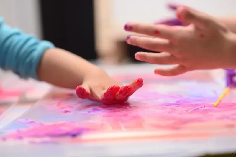 Kids' finger painting activity, a close up of their hands covered in red paint.