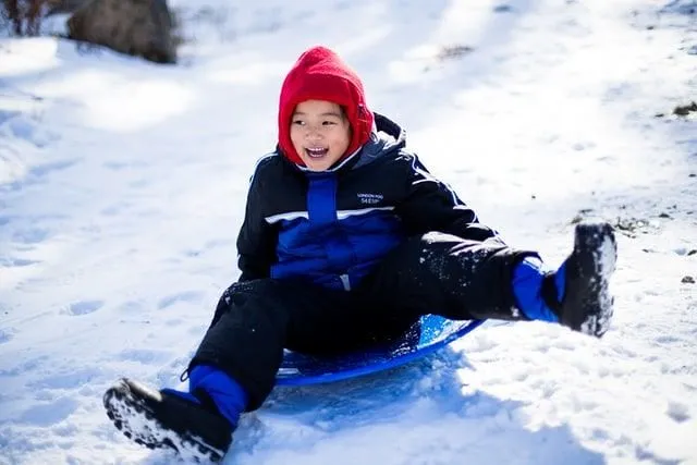 Young boy on a toboggan smiling as he slides down the hill on the snow.
