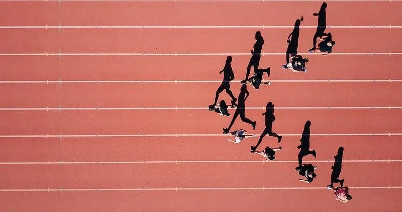 Runners on an athletics track, on a sunny day, their shadows on the track. 