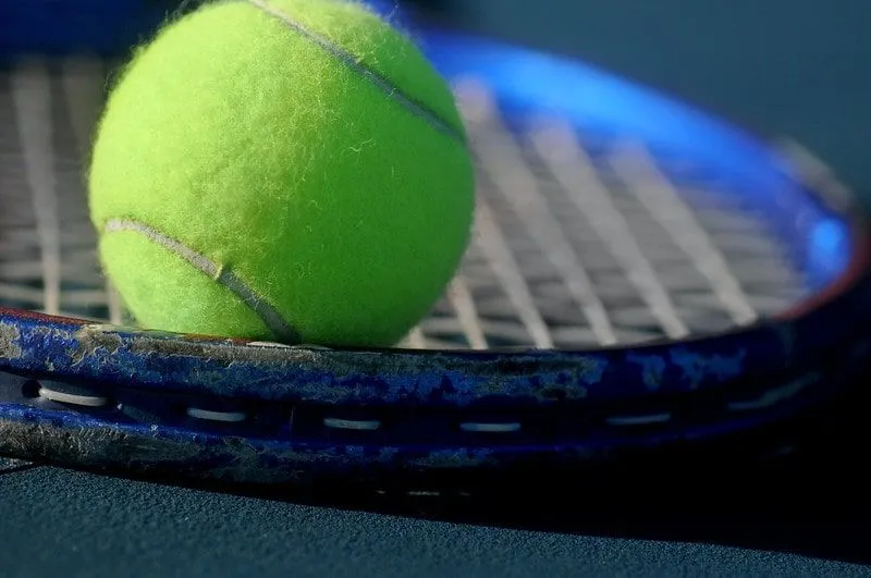 Close up of a tennis ball on the strings of a blue tennis racquet.y