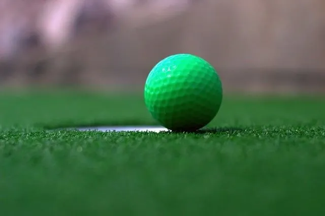 Close up of a green golf ball on the edge of the hole on the golf course.
