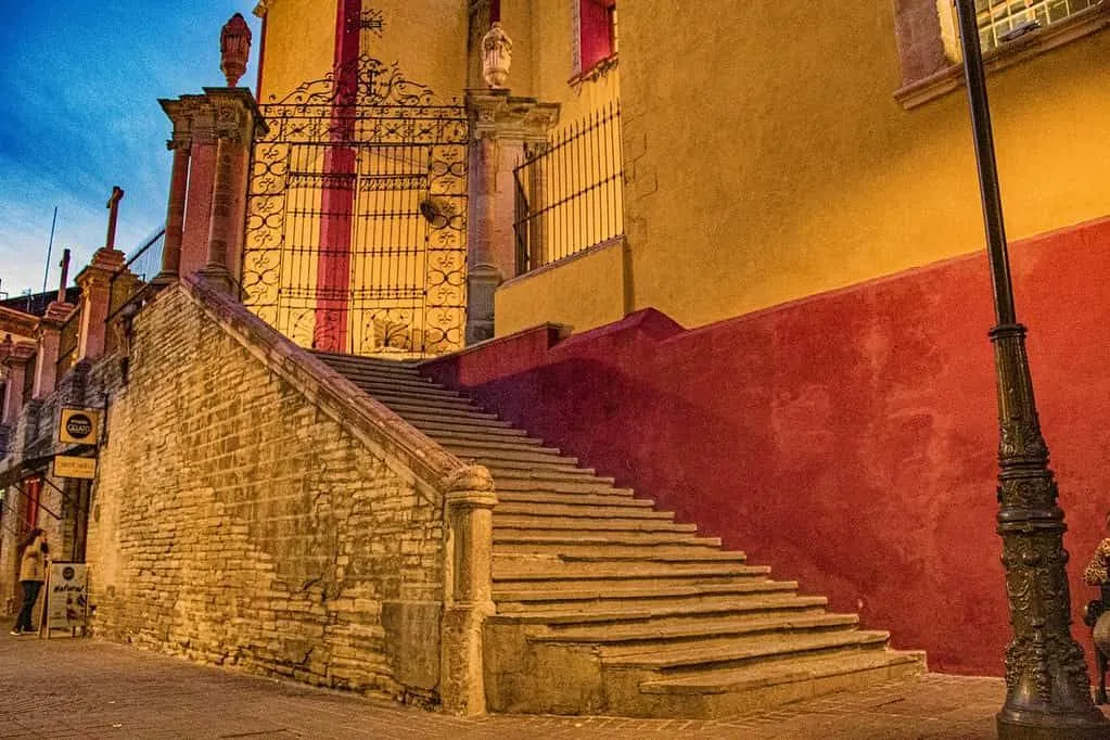 Colourful architecture in Mexico City: a staircase leading up to a gate of a red and yellow building.