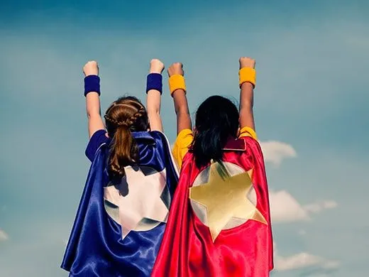 Two young girls dressed in Captain Marvel costumes pretending to fly away.