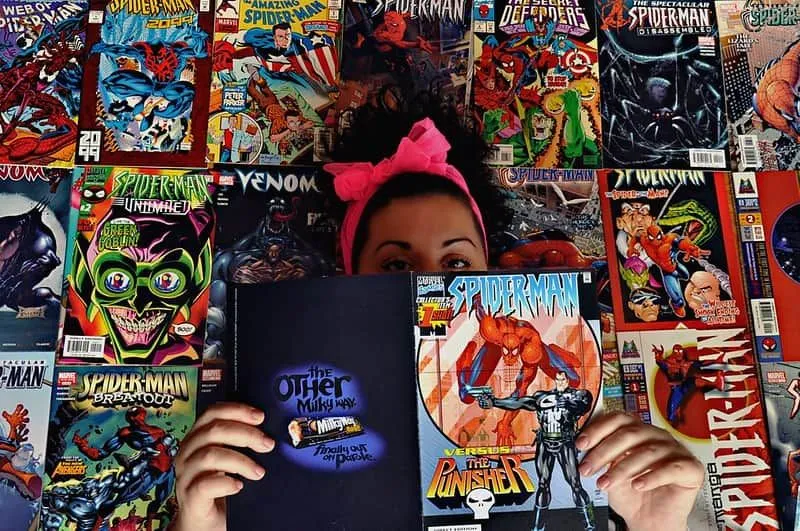 Girl standing in front of rows of Marvel comic books holding a Spiderman comic open in front of her face.