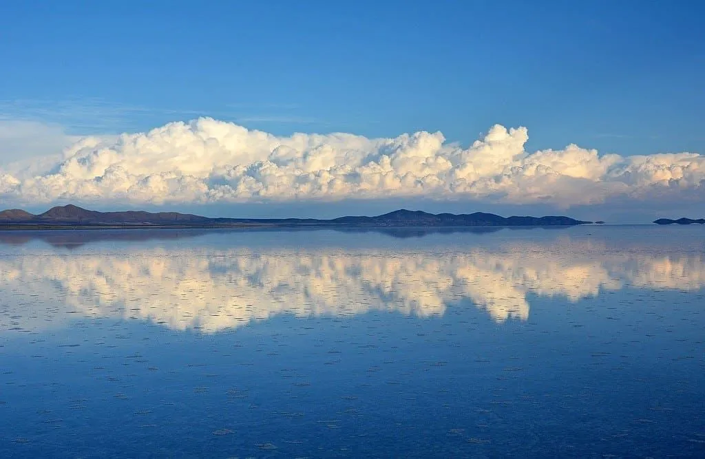 Bolivian landscape skyline mirrored in the lake, hills with a cloudy blue sky above.