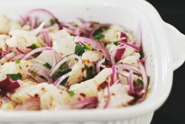 Dish of  white fish ceviche with red onions and chilli flakes.