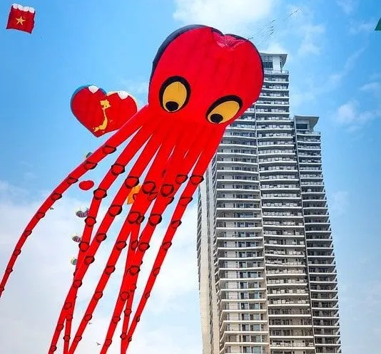 Giant inflatable octopus being pulled through the sky, a tall skyscraper behind it.