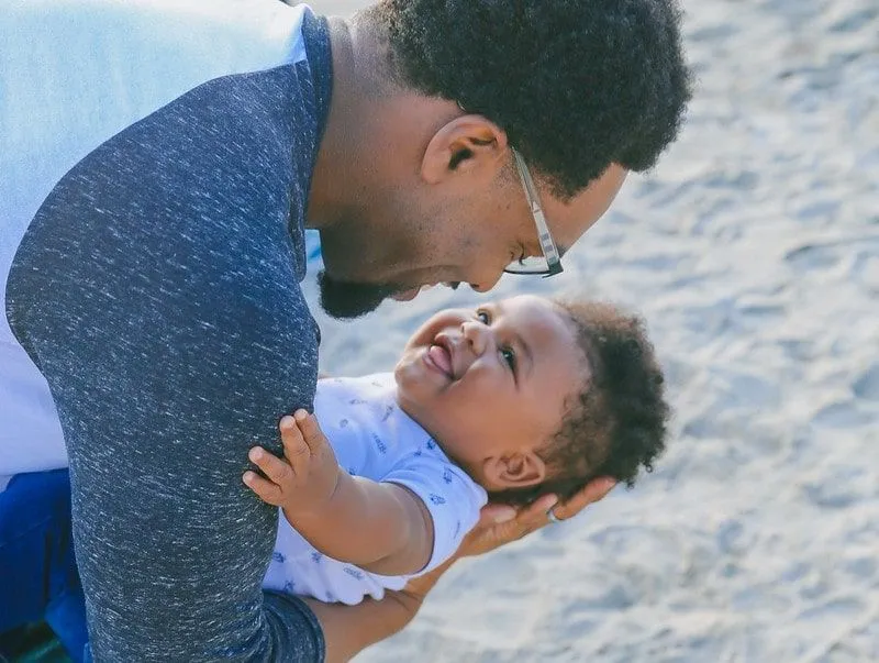 Dad holding baby on the beach, both smiling at each other.