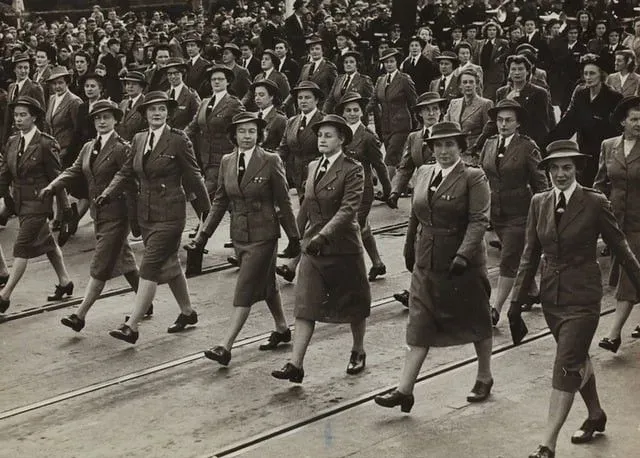A black and white picture of many women in uniform marching for VE day.