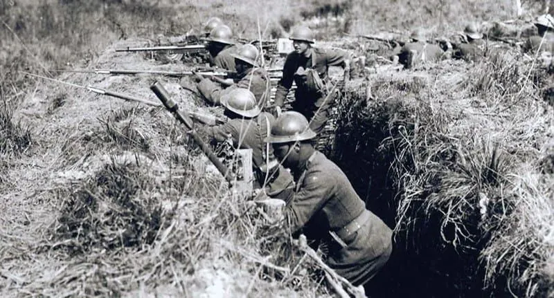 A black and white photo of soldiers in trenches aiming their guns.s