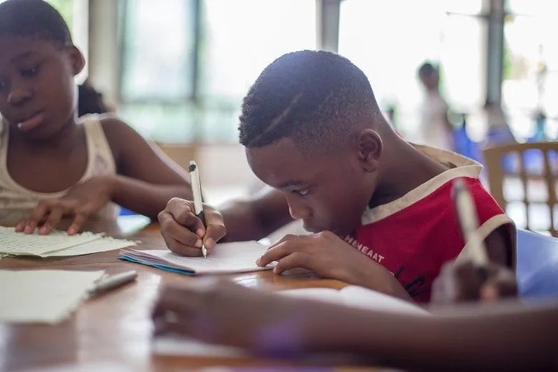 Young boy at his desk in school writing out improper fractions in workbook.
