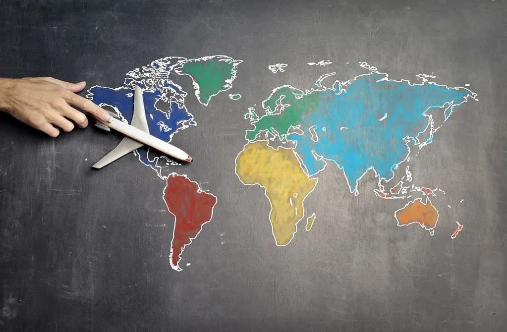 Map of the world drawn on a blackboard, the teacher moves a toy plane across it.