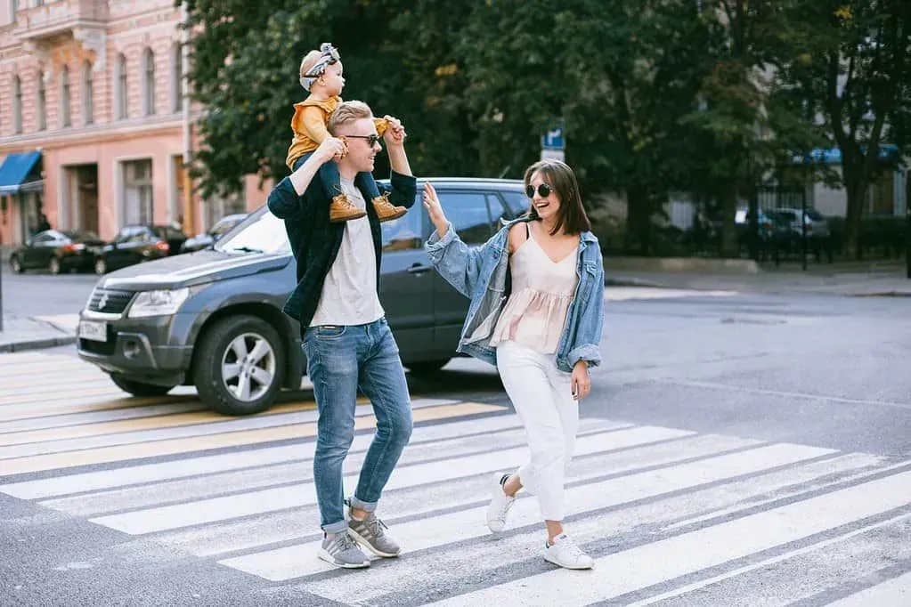Parents crossing the road with their baby girl on her dad's shoulders.