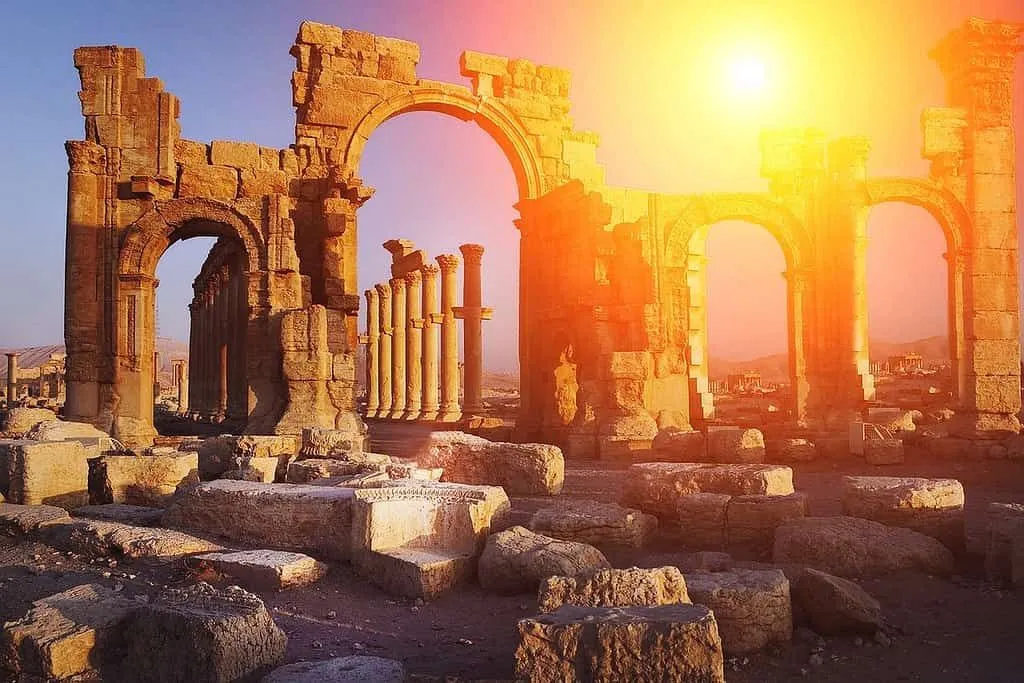 Roman ruins with an orange sun shining behind, giving them a divine appearance.