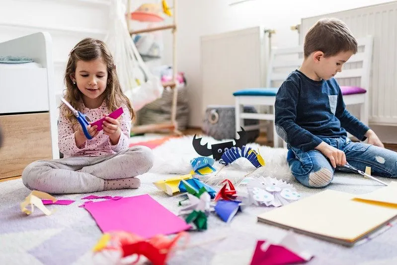 Little girl and boy sat on the floor making origami gift boxes.