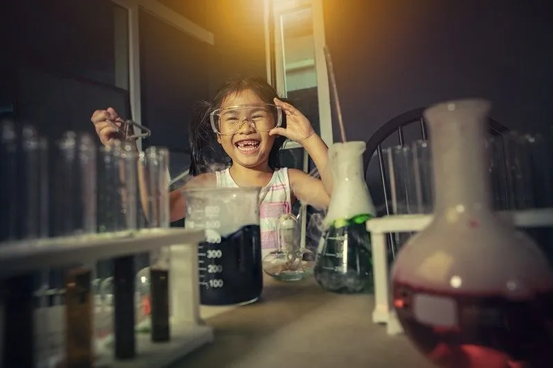Little girl wearing goggles, laughing while doing a chemistry experiment.
