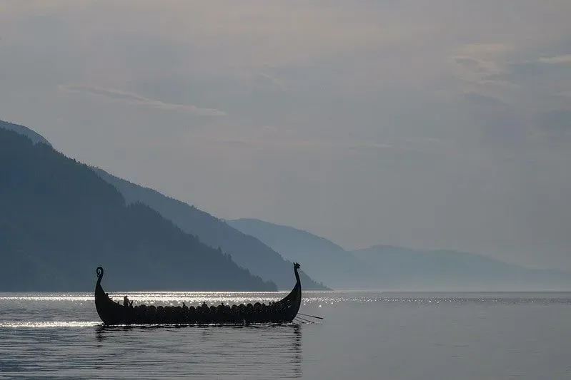 A Viking crafted boat on a lake with mountains surrounding.
