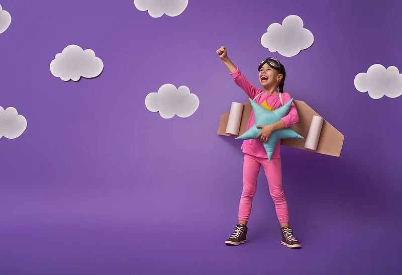 Little girl wearing a homemade astronaut costume with cardboard wings pretending to soar into the sky.