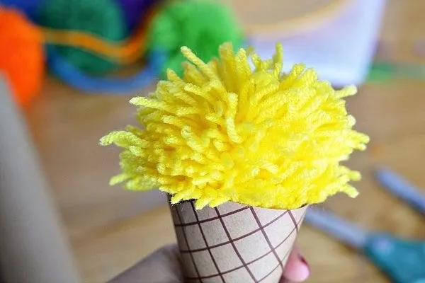 An ice cream cone made from paper with a pom pom as the ice cream scoop.