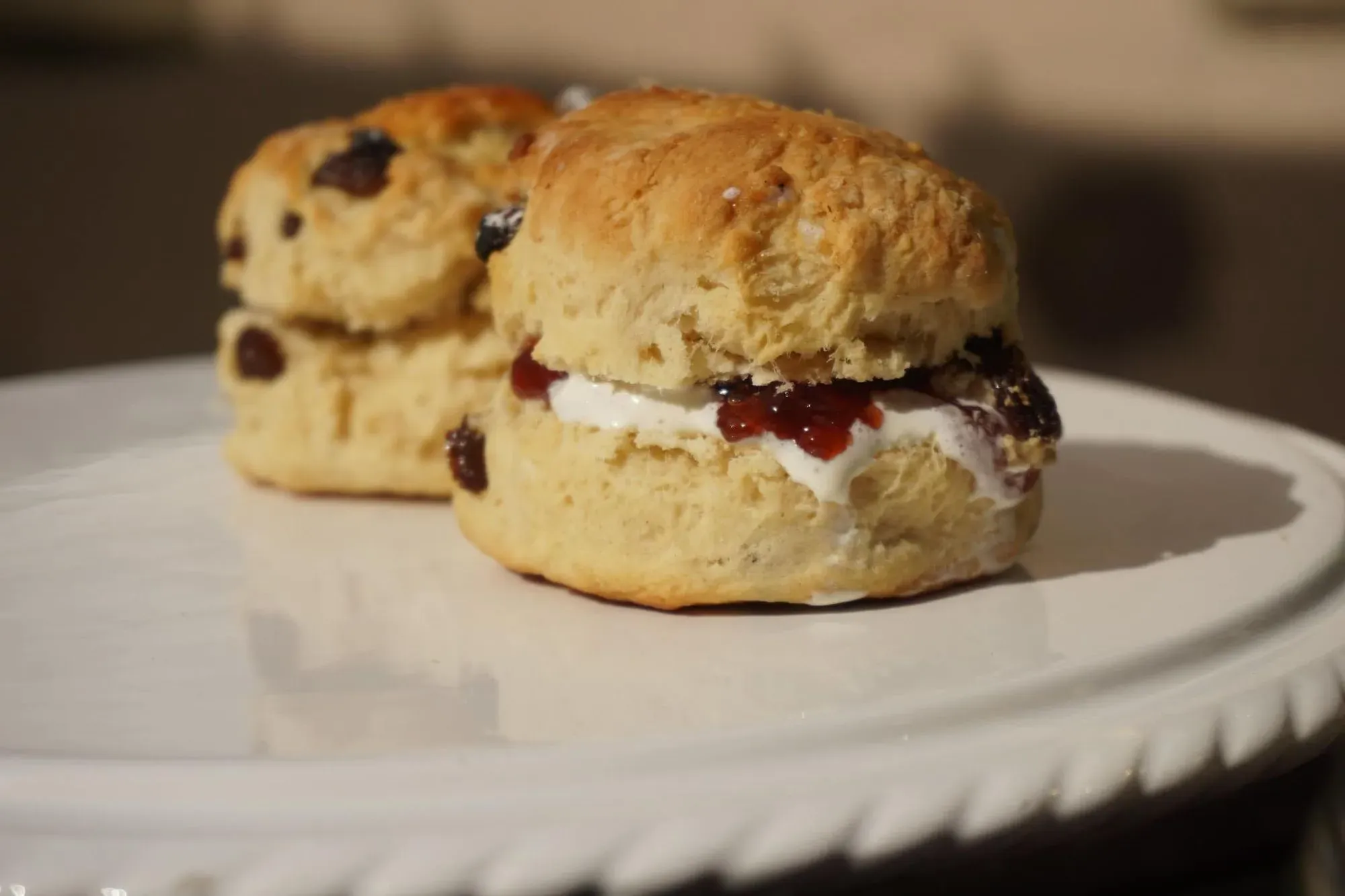 Fruit scones with clotted cream and jam on a plate.